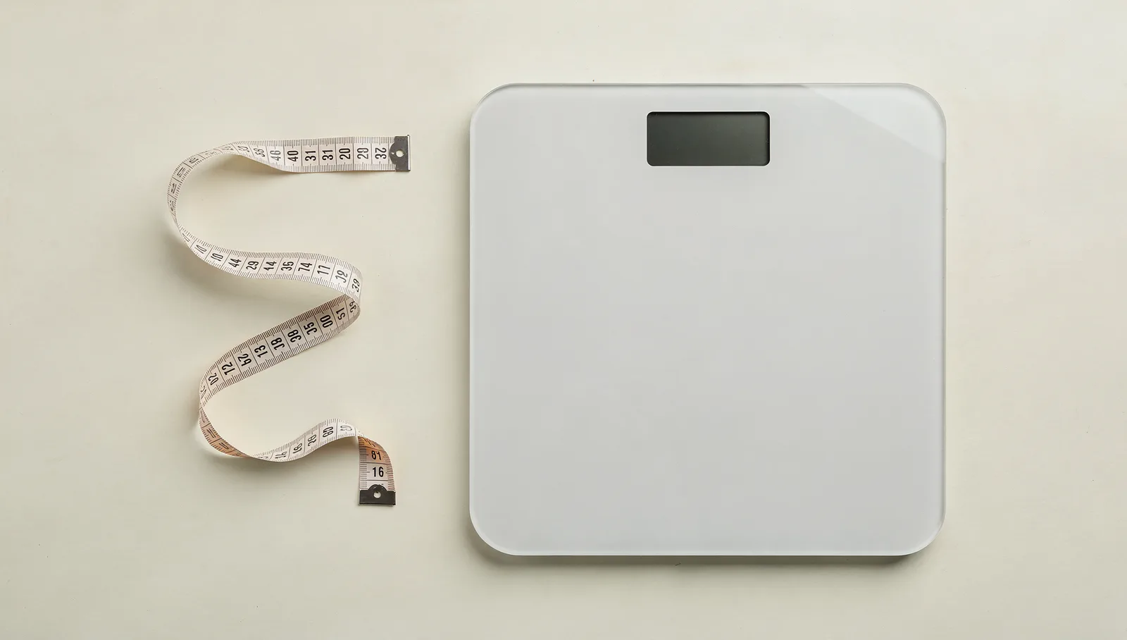A flat digital floor scale and a cloth measuring tape on a plain pale surface, seen from directly overhead